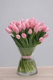 Photo of Bouquet of beautiful pink tulips in vase on wooden table against grey background