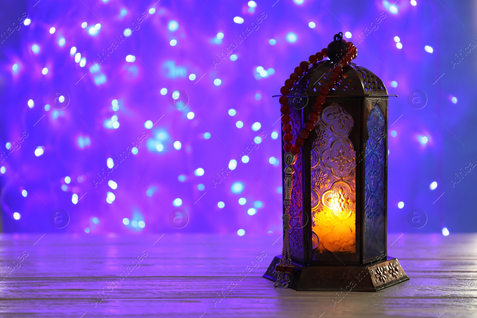 Photo of Muslim lamp with candle on table against blurred fairy lights. Fanous as Ramadan symbol