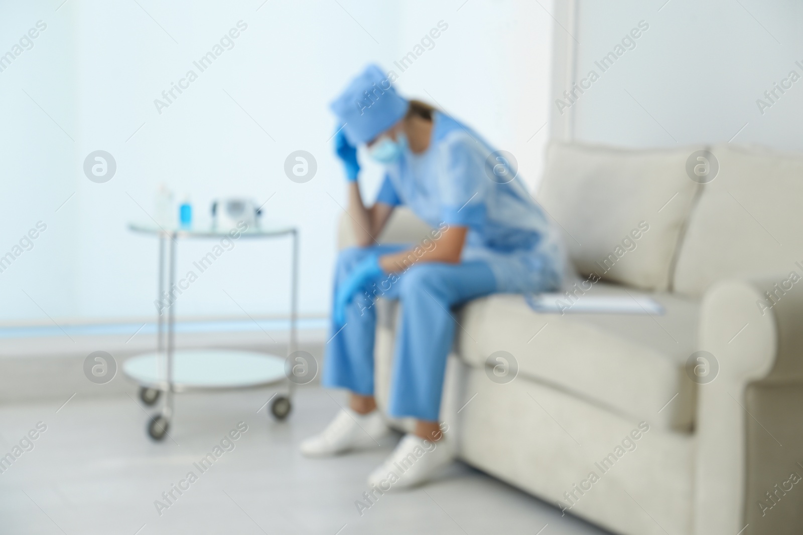 Photo of Exhausted doctor sitting on sofa indoors, blurred view. Stress of health care workers during COVID-19 pandemic