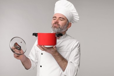 Chef in uniform with cooking pot on grey background