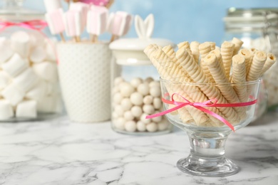 Photo of Vase with wafer rolls and other sweets on white marble table, space for text. Candy bar