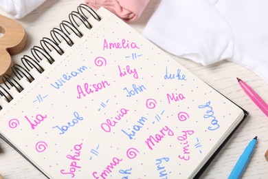 Notebook with different baby names and child's items on white wooden table, closeup