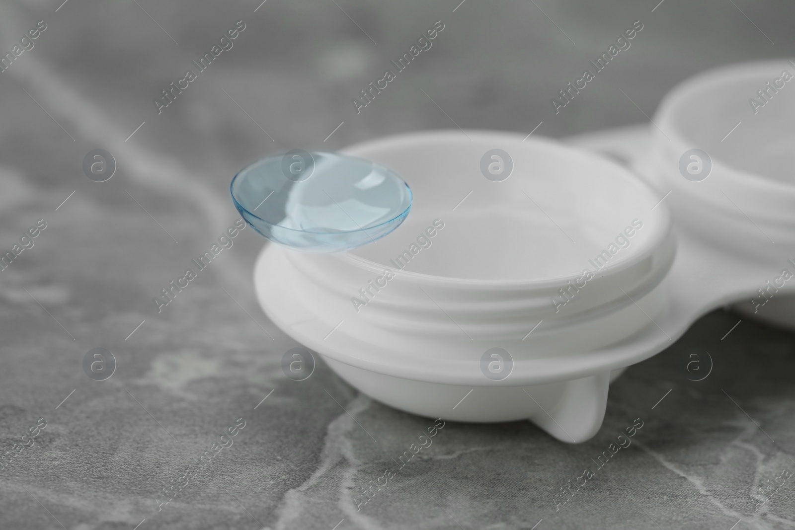 Photo of Case with contact lens on light grey marble table, closeup