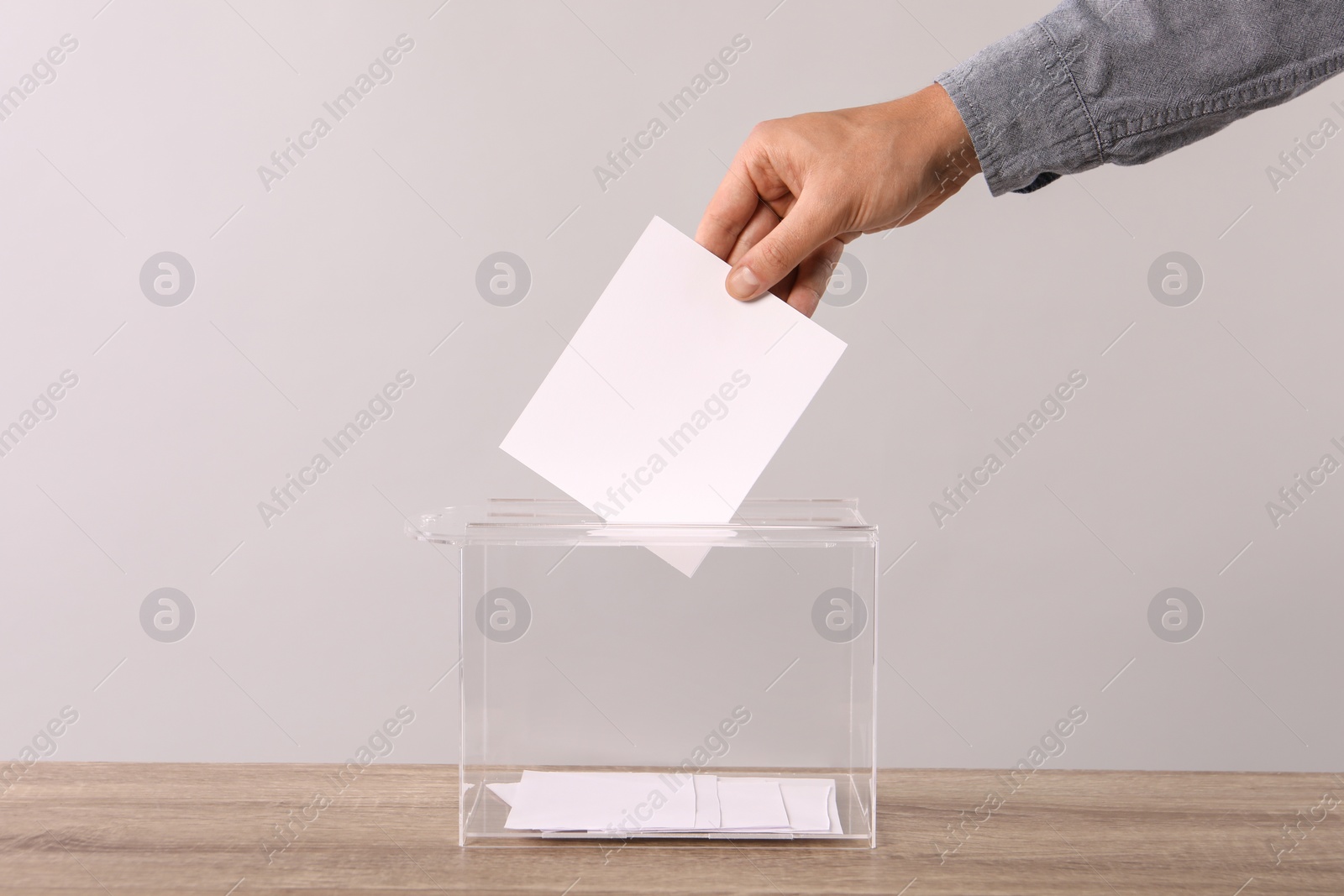 Photo of Man putting his vote into ballot box on light grey background, closeup