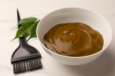 Bowl of henna cream and brush on white marble table, closeup. Natural hair coloring