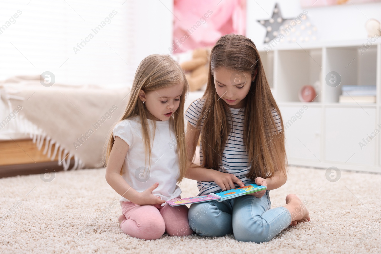 Photo of Cute little sisters reading book together at home