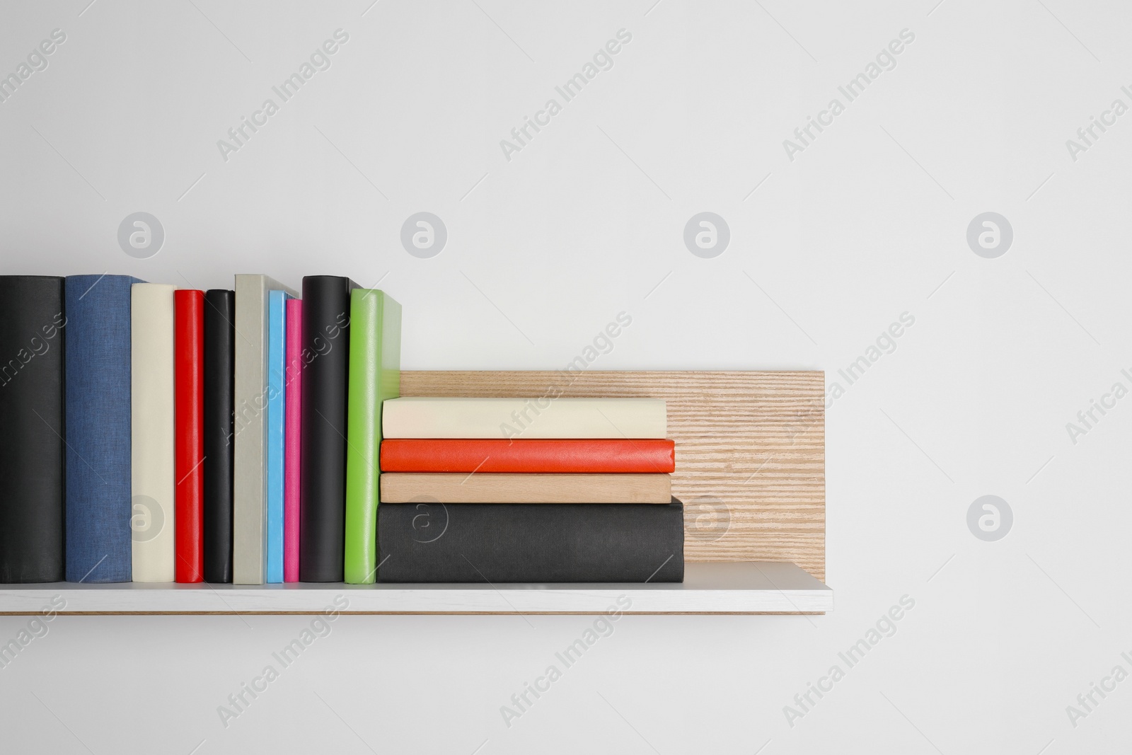 Photo of Different books on wooden shelf near white wall, space for text