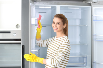 Photo of Woman in rubber gloves cleaning empty refrigerator at home