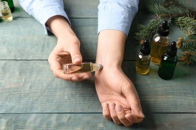 Photo of Woman applying essential oil on wrist at wooden table, closeup