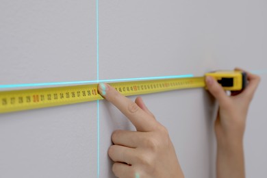 Photo of Woman using cross line laser level and tape for accurate measurement on grey wall, closeup