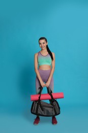 Beautiful woman with sports bag and yoga mat on light blue background