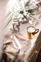 Photo of Golden cupcocoa and Christmas decor on window sill indoors