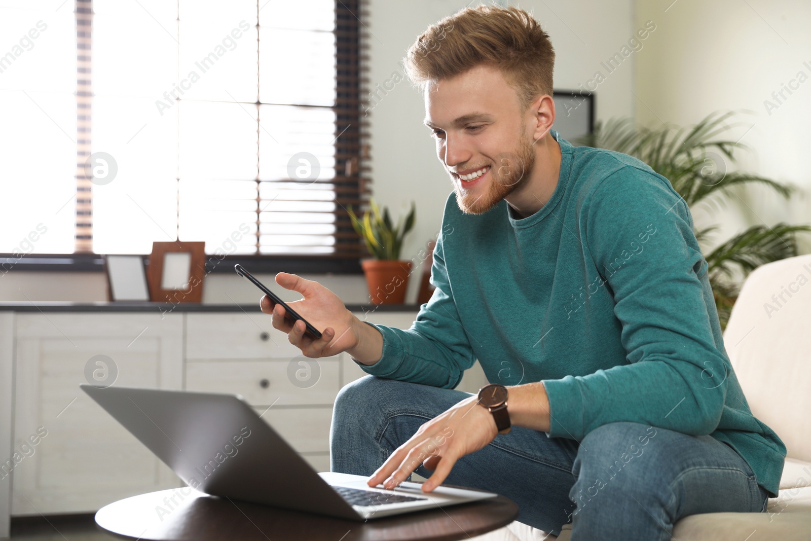 Photo of Young man using smartphone and laptop in living room