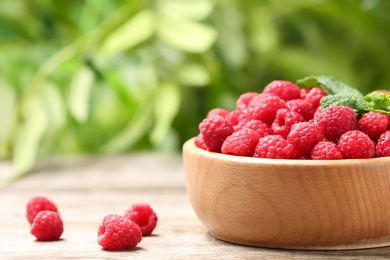 Photo of Bowl with ripe aromatic raspberries on table against blurred background