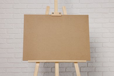 Wooden easel with blank board near white brick wall