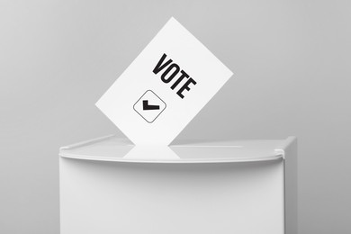 Image of Paper with word Vote and tick sticking out of ballot box on light grey background