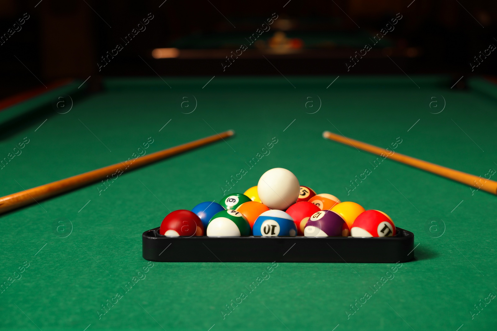 Photo of Plastic triangle rack with billiard balls and cues on green table indoors