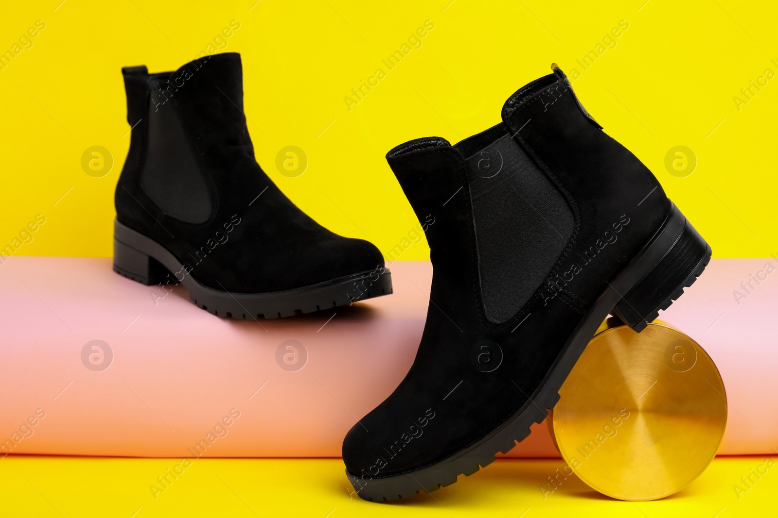 Photo of Stylish black female boots and decor on yellow background