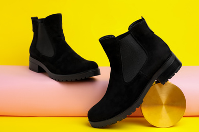 Stylish black female boots and decor on yellow background