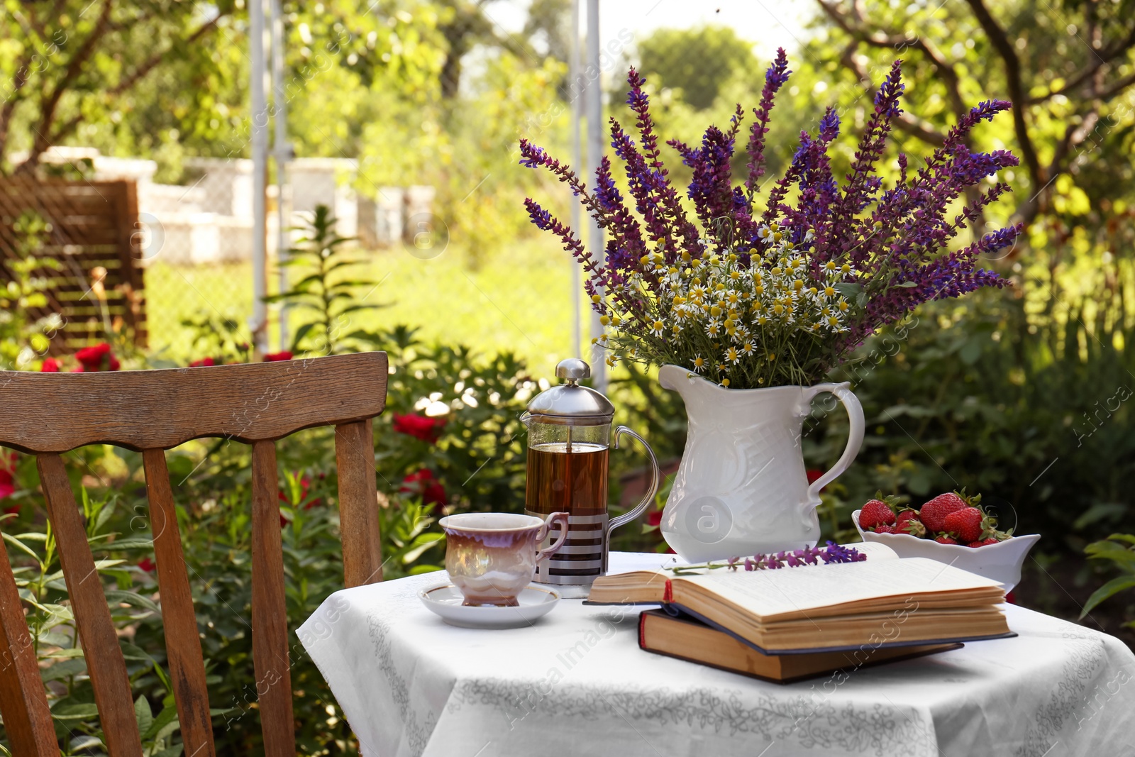 Photo of Beautiful bouquet of wildflowers and books on table served for tea drinking in garden