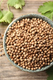 Photo of Dried coriander seeds in bowl and green leaves on wooden table, flat lay