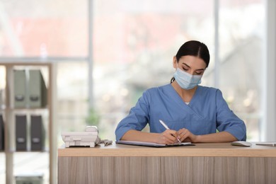 Photo of Receptionist with protective mask working at countertop in hospital