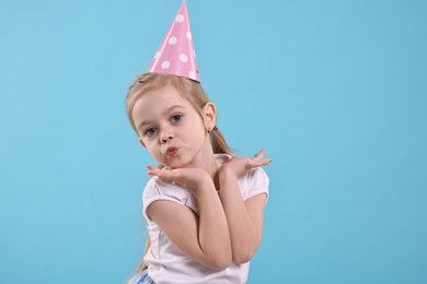 Birthday celebration. Cute little girl in party hat on light blue background