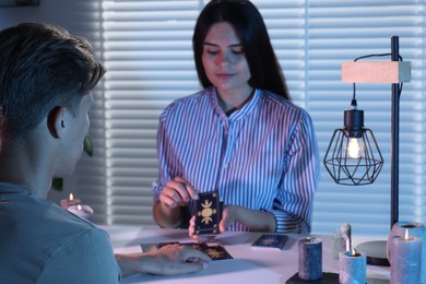 Astrologer predicting client's future with tarot cards at table indoors