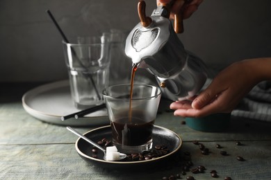 Woman pouring coffee from moka pot into glass at rustic wooden table, closeup