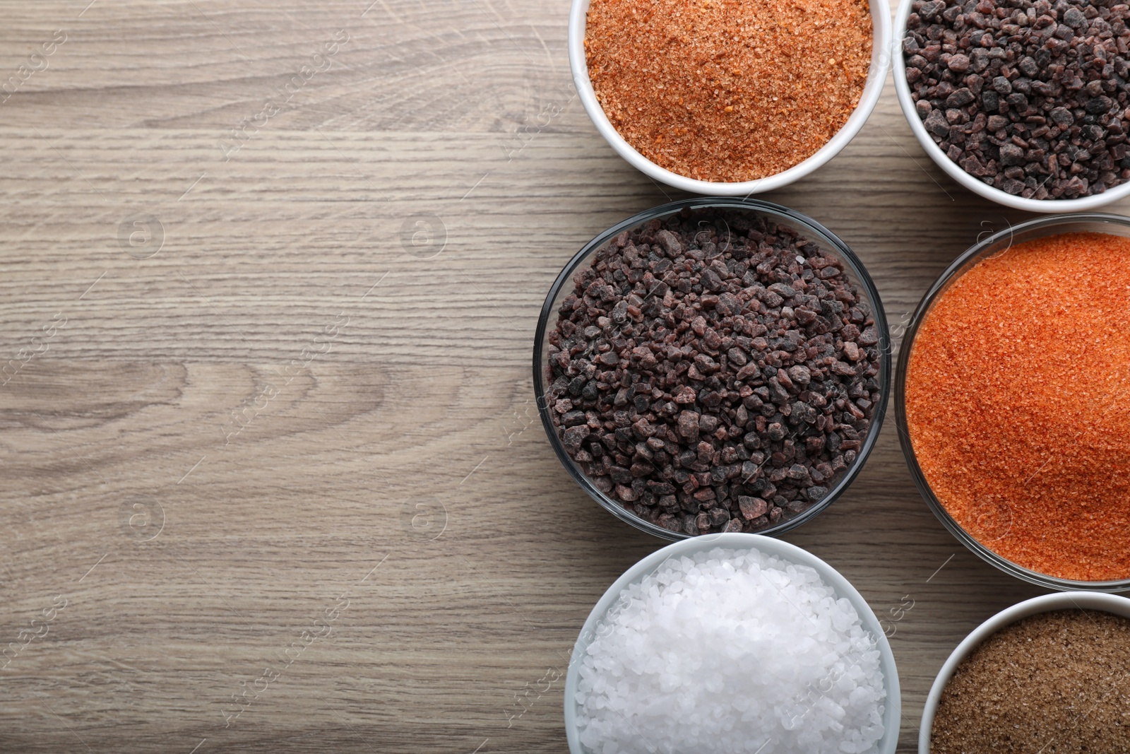 Photo of Different kinds of salt on wooden table, flat lay. Space for text