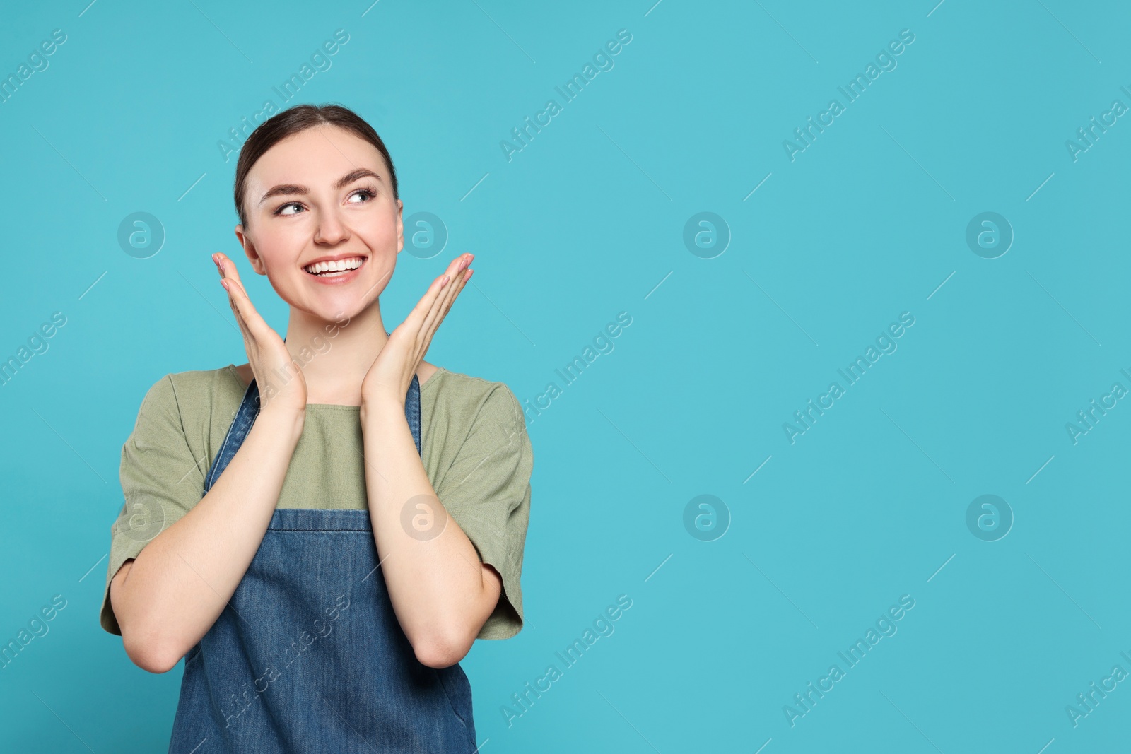 Photo of Beautiful young woman in clean denim apron on light blue background. Space for text