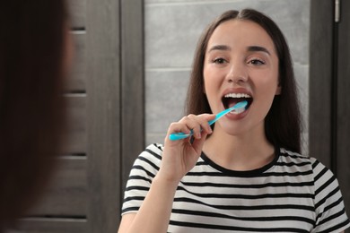 Young woman brushing her teeth with plastic toothbrush near mirror in bathroom