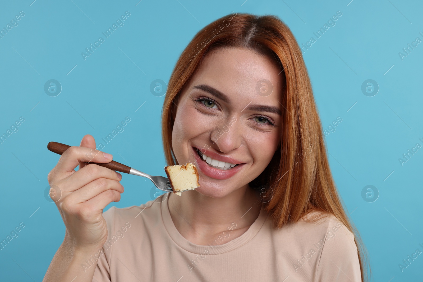 Photo of Young woman eating piece of tasty cake on light blue background