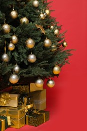 Photo of Beautifully decorated Christmas tree and many gift boxes on red background, closeup