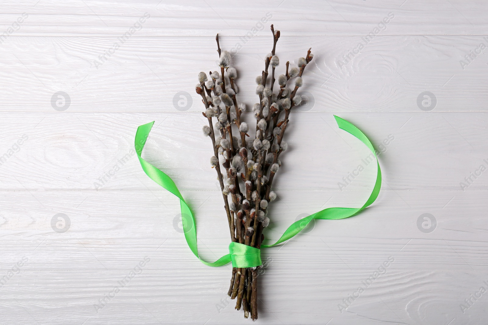 Photo of Beautiful blooming willow branches with green ribbon on white wooden table, top view