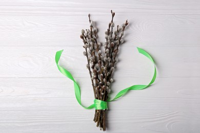 Photo of Beautiful blooming willow branches with green ribbon on white wooden table, top view