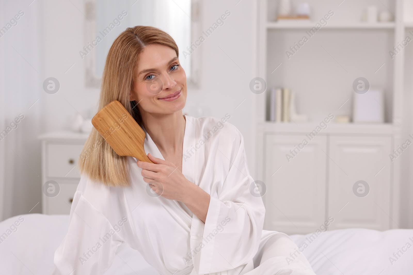 Photo of Beautiful woman brushing her hair on bed in room