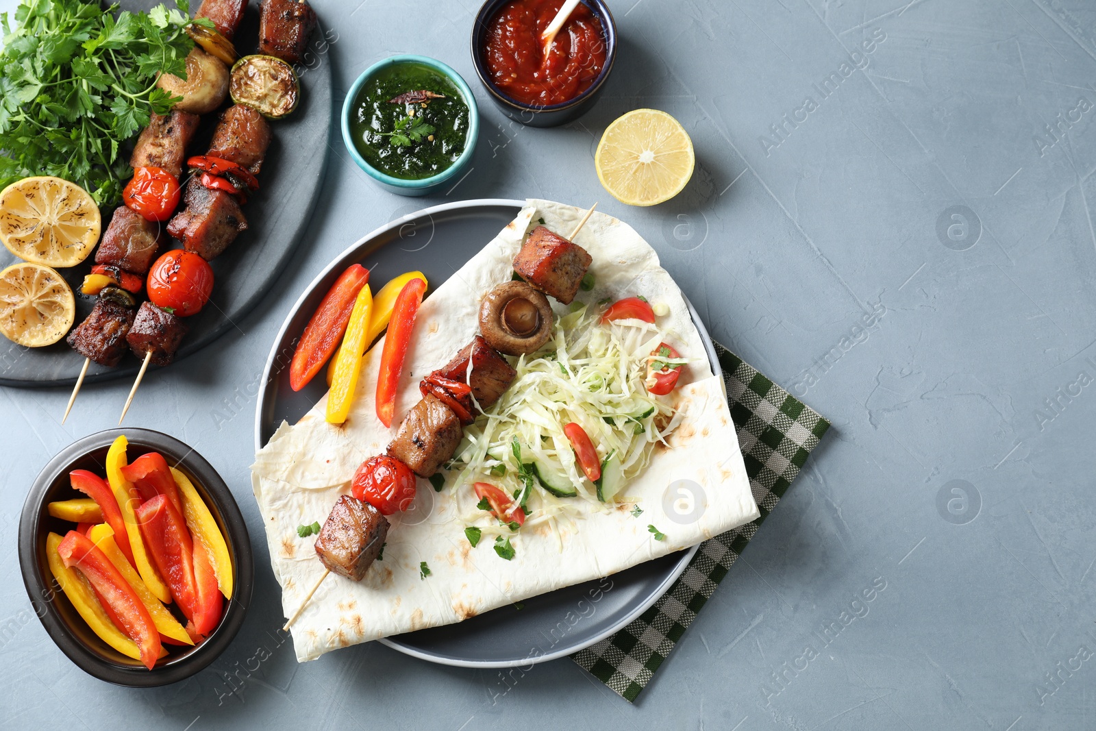 Photo of Delicious shish kebabs with vegetables served on gray table, flat lay