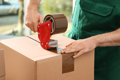 Man packing box with adhesive tape indoors, closeup. Moving service