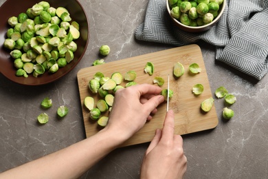 Photo of Woman cutting fresh Brussels sprouts on wooden board, top view