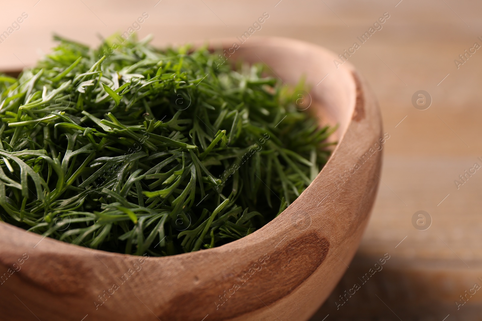 Photo of Fresh cut dill in wooden bowl on table, closeup