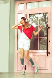 Happy girl with retro roller skates standing near pink door