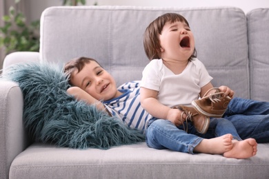 Photo of Cute little boy and his crying baby sister on sofa at home