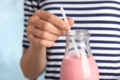 Woman with glass bottle of tasty smoothie on light blue background, closeup