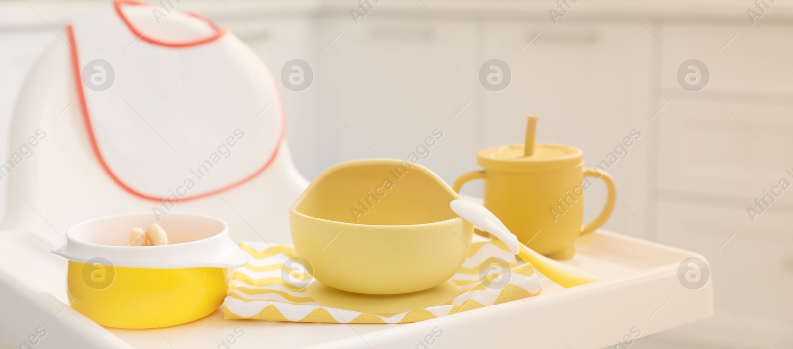 Image of High chair with set of baby tableware on tray indoors, closeup view. Banner design