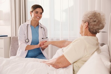 Photo of Young caregiver talking to senior woman in bedroom. Home health care service