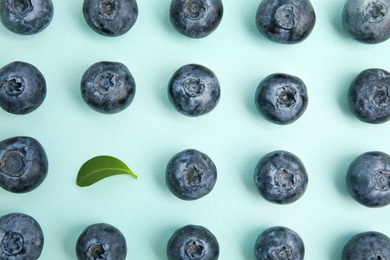 Photo of Fresh ripe blueberries and leaf on light blue background, flat lay