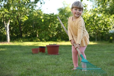 Photo of Cute little girl with rake in garden on spring day
