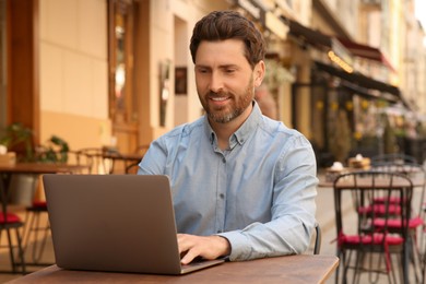 Photo of Man working on laptop at table in outdoor cafe