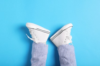 Photo of Little baby in stylish gumshoes on light blue background, top view